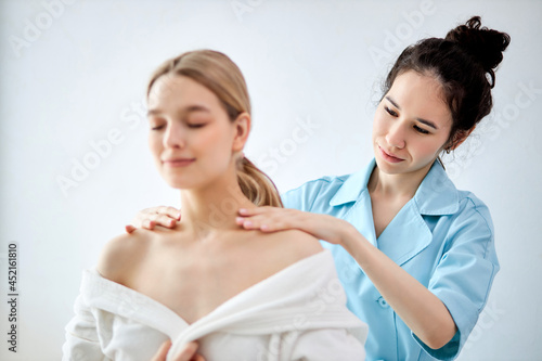 Charming Lady Getting Neck Massage In Beauty Spa. Caucasian Female Relaxing In Spa While Getting Neck Massage. Serene Woman In Beauty Center, Wearing White Bathrobe. Focus on masseur