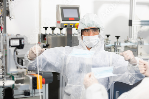 male engineers wearing personal protective equipment uniform(PPE) wearing medical face mask, producing medical face masks and checking machine in laboratory