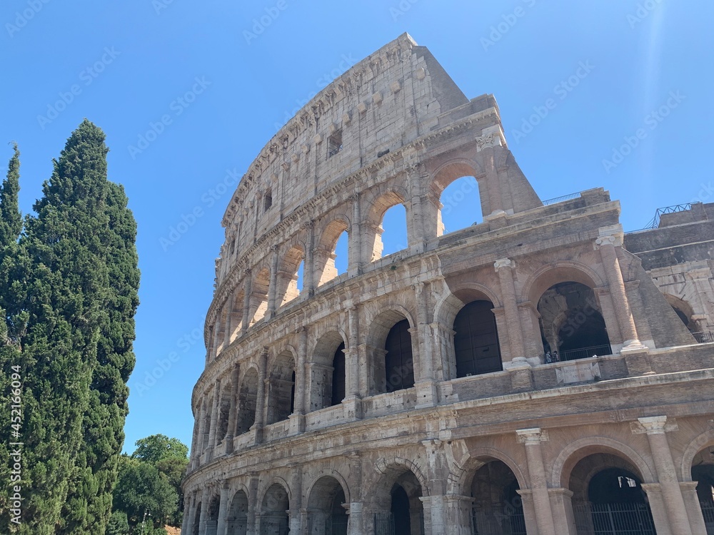Close up view of the Colosseum amphitheatre at Roma city centre next to the Roman Forum. Tall and green Italian cypress tress grows beside. Famous sightseeing and tourism place. Rome, Lazio, Italy.