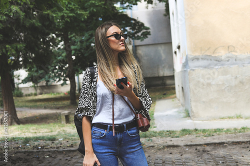 Young girl on the street is waiting for someone and typing a message.