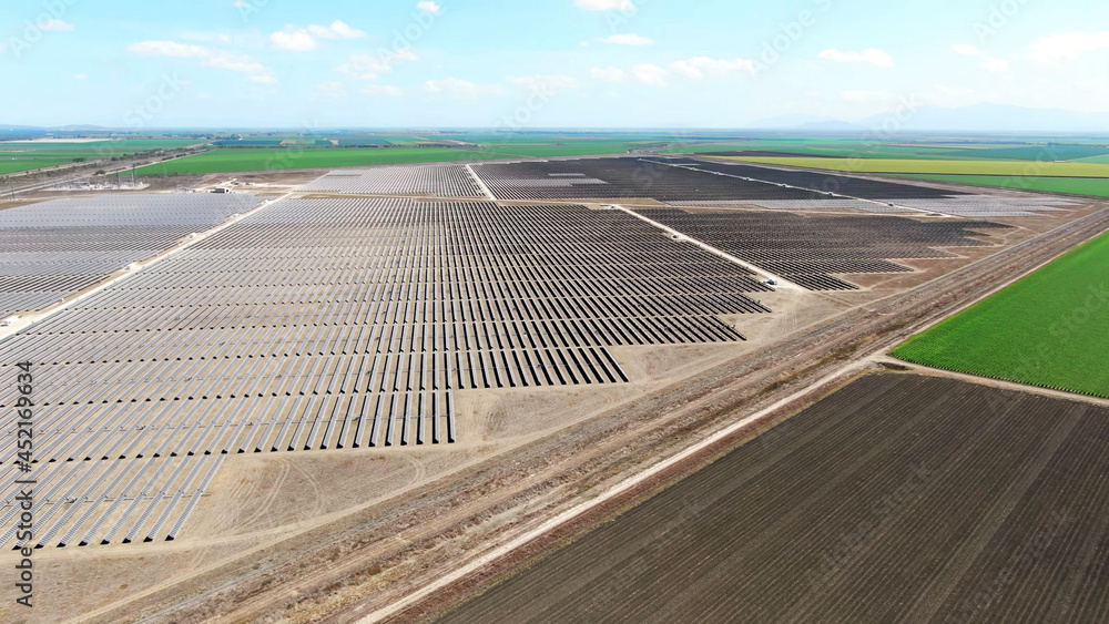 Fototapeta premium drone aerial view of vast solar energy farm with plowed agriculture fields in the countryside.