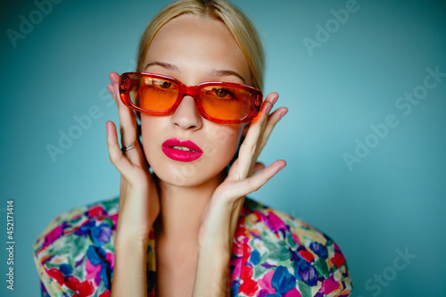 Fashionable  woman wearing trendy oval orange sunglasses, posing on blue background. Close up fashion portrait. Copy, empty space for text