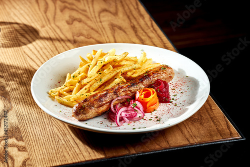 Grilled sausages with fries in a white plate on a wooden table. Currywurst