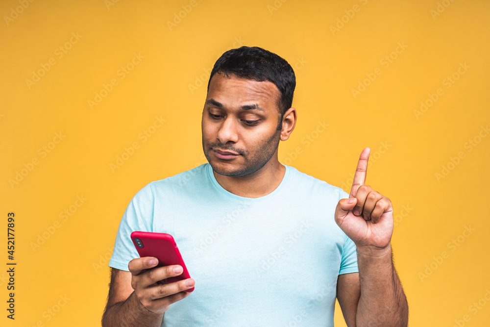 Portrait of handsome excited cheerful joyful indian african american guy wearing casual sending and getting messages to his lover isolated over yellow background. Using phone. Pointing finger. Portrait of handsome excited cheerful joyful indian african american guy wearing casual sending and getting messages to his lover isolated over yellow background. Using phone. Pointing finger.