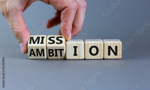 Do your mission with ambition. Businessman turns wooden cubes and changes the word 'mission' to 'ambition'. Beautiful grey table, grey background, copy space. Business, mission or ambition concept.