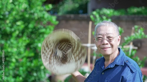 senior asian farmer using hat to blow air during hot weather