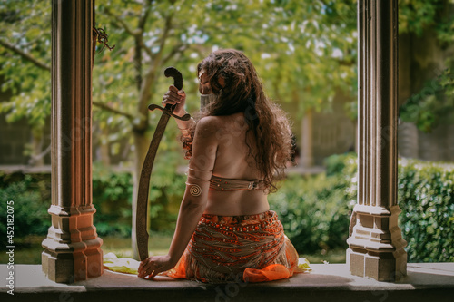 Young belly dancer sitting in Olite castle with a Arabian saber
