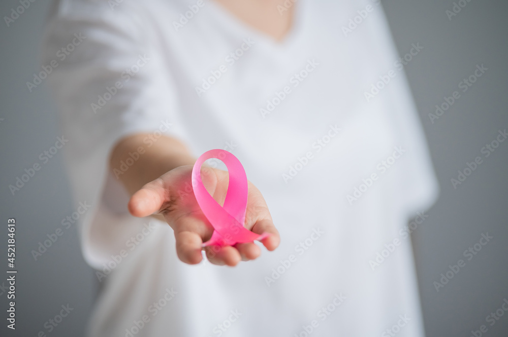 A faceless woman wearing a white t-shirt holds a pink ribbon as a symbol of breast cancer on a white background. A faceless woman wearing a white t-shirt holds a pink ribbon as a symbol of breast cancer on a white background.