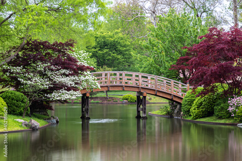 Fényképezés Arching wooden bridge spans across the lake from shore to island, in Japanese garden