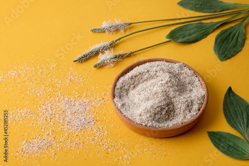 Psyllium, isfagula plant product is the husk of plantain seeds in a plate on a yellow background. Useful dietary supplement, superfood. Top view, horizontal orientation, without people, copy space. 