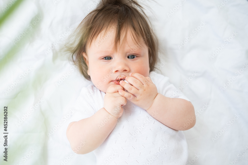 cute baby girl 6 month with nipple lying on a white bedding at home. top view. cute baby girl 6 month with nipple lying on a white bedding at home. top view.