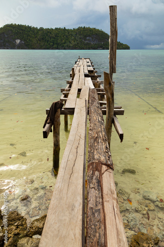 A rudimentary wooden jetty, half broken, stands on the sand near the beach, Friwin Island, Raja Ampat, West Papua photo