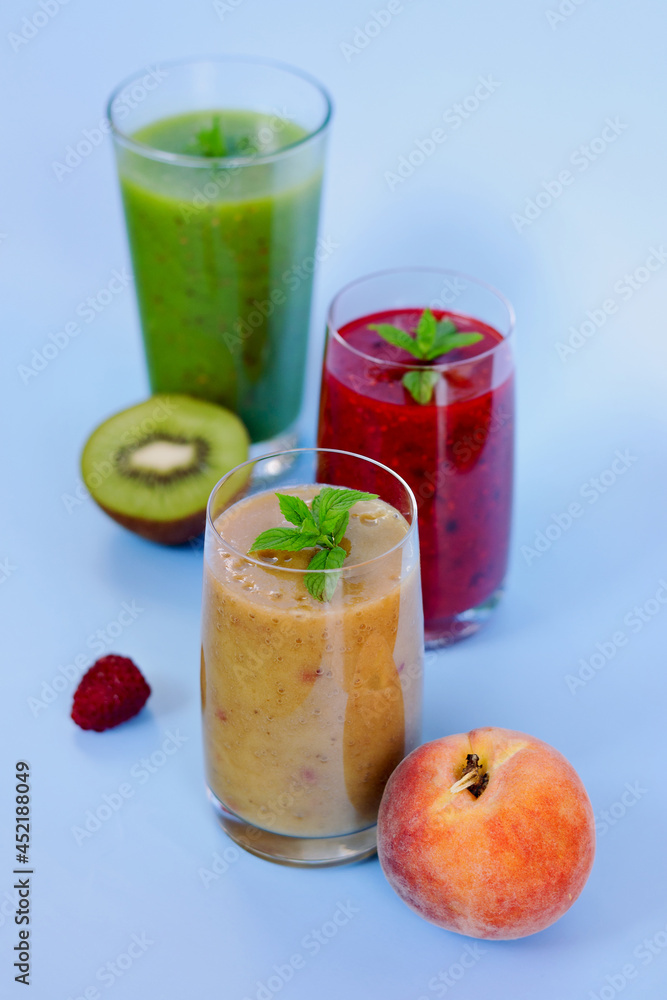 Top view of three different fresh delicious smoothies in a glasses made of peach, banana and berries with mint. Creative concept of healthy detox drink, diet or vegetarian food concept. Copy space. Top view of three different fresh delicious smoothies in a glasses made of peach, banana and berries with mint. Creative concept of healthy detox drink, diet or vegetarian food concept. Copy space.