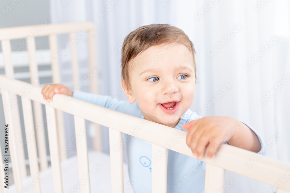 a happy baby boy in a crib in the children's room is holding on to the side and smiling a happy baby boy in a crib in the children's room is holding on to the side and smiling