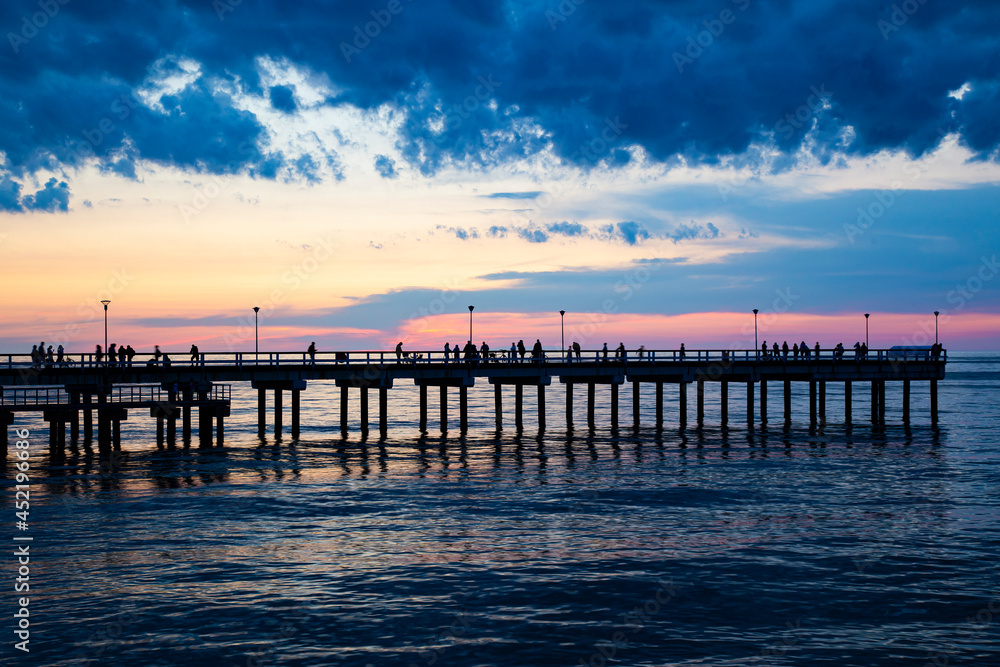 silhouette of palanga pier with people in baltic sea during beautiful sunset with clouds