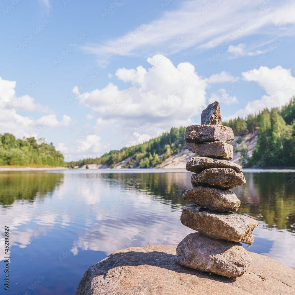 Stacked stones in a pyramide near blue lake with rocks and cloudy sky Stacked stones in a pyramide near blue lake with rocks and cloudy sky