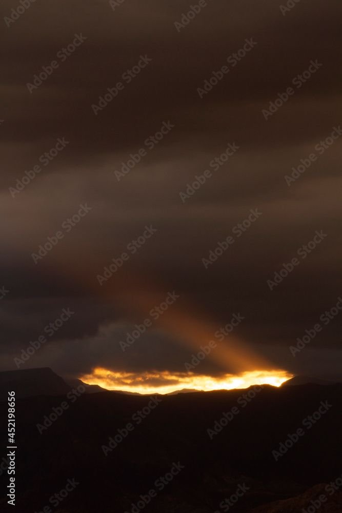 Dark cloudscape. View of the dramatic sunset with dark clouds. The last bright ray of sunlight strikes across the sky and mountains silhouette.