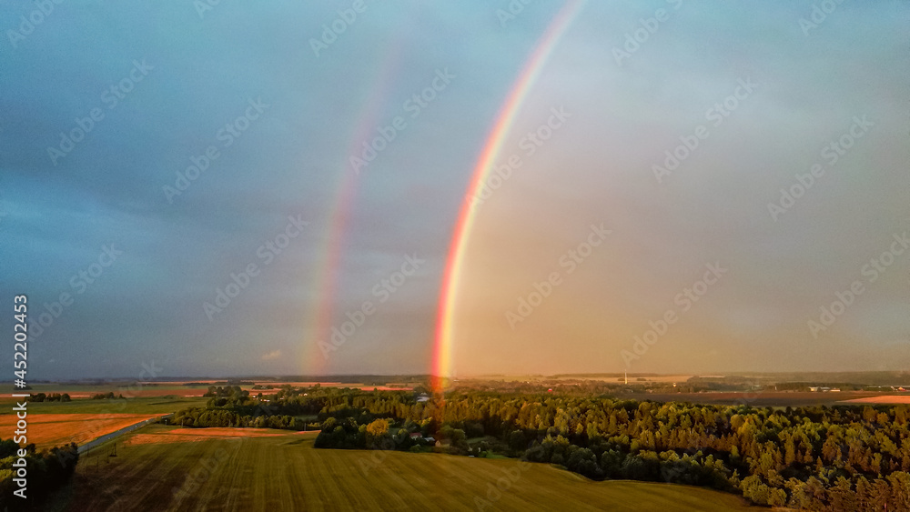 Double Rainbow Over Forest and Wheat Field. Dark Thunderstorm Clouds and Rainbow Over Rural Highway Road Landscape. Camera Moves Backward. Aerial Shot Double Rainbow Over Forest and Wheat Field. Dark Thunderstorm Clouds and Rainbow Over Rural Highway Road Landscape. Camera Moves Backward. Aerial Shot