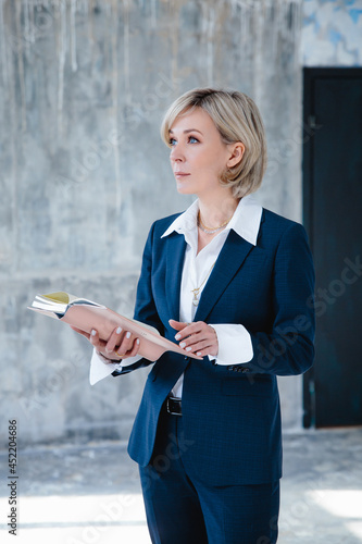 A beautiful business woman in a business suit poses with a notebook in her hands
