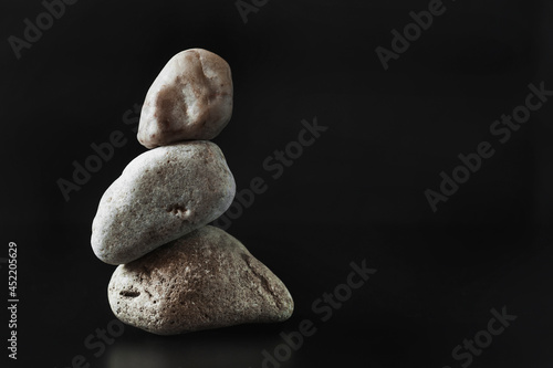 Three stones stand on top of each other keeping their balance. Dark background. Copy space..