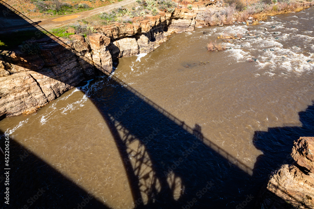 The historic Salt River Bridge casts it's shadow over the Salt River swollen from snow melt from the White Mountains. East Central Arizona.

