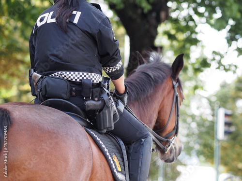 Oslo, Norway - 01.05.2021: Female police offer riding on a horse with gun in focus