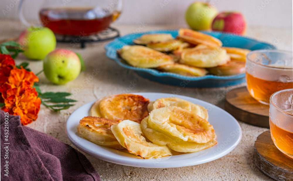 Dessert, fried rings of apples in batter on a white plate on a light concrete background. Apples recipes. Dessert, fried rings of apples in batter on a white plate on a light concrete background. Apples recipes.