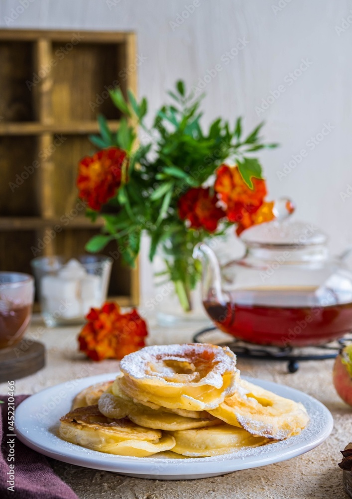 Dessert, fried rings of apples in batter on a white plate on a light concrete background. Apples recipes. Dessert, fried rings of apples in batter on a white plate on a light concrete background. Apples recipes.