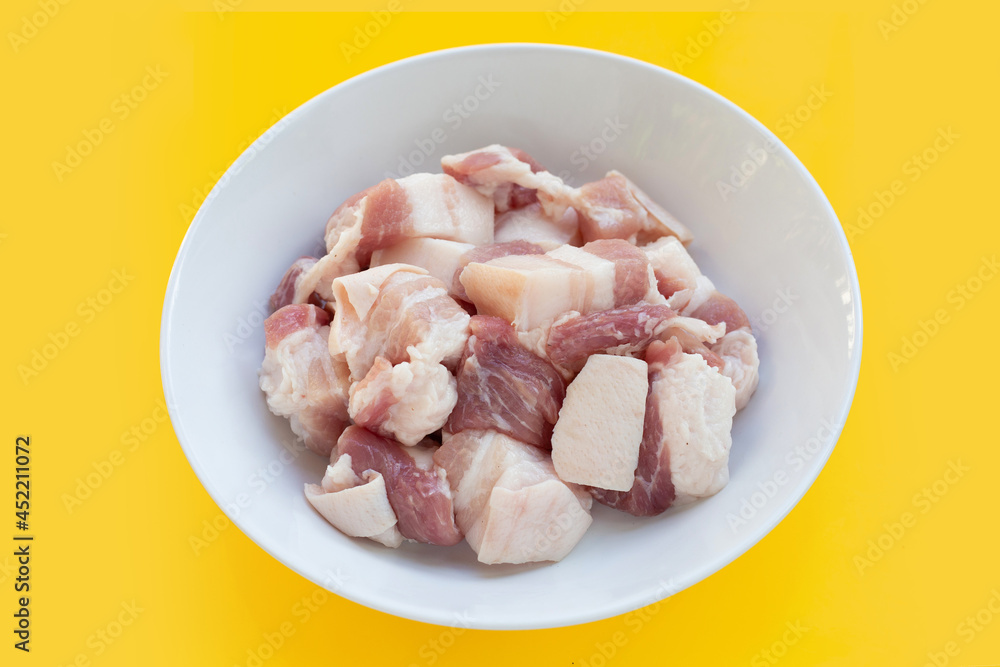 Cut streaky pork in white bowl on yellow background.