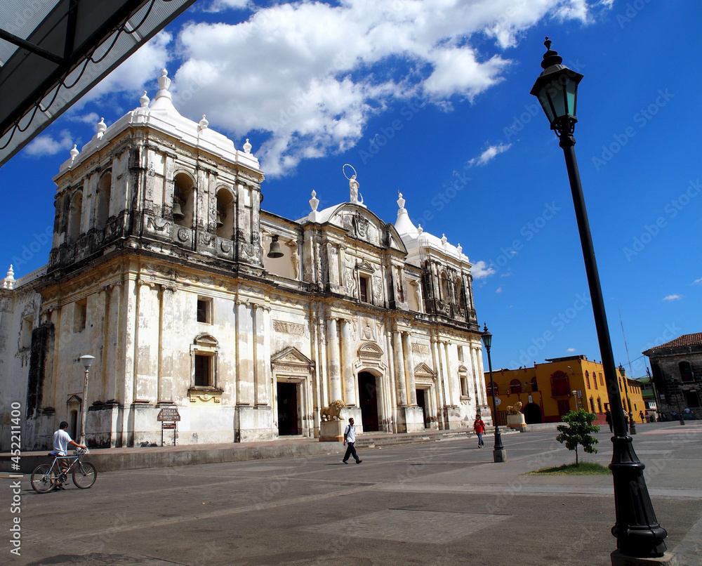 Leon, Nicaragua, cathedral in the main square of Leon. Blue sky, sunny with clouds, street scene with people walking and bicycle