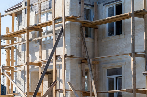 Residential country house under construction. Construction of cottage in final stage. Wooden scaffolding with facade bricks