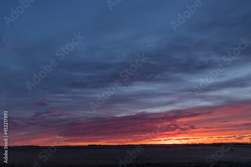 Dramatic sunrise or sunset in red, orange, and blue over an open field