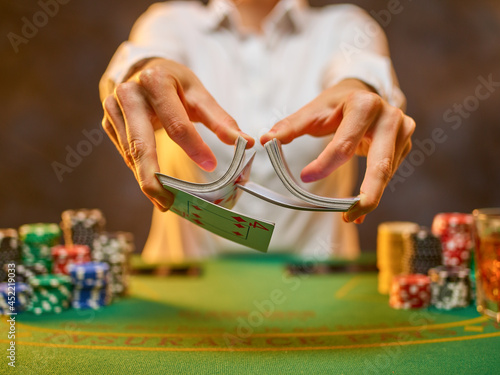 Poker club, casino. The dealer shuffles the cards professionally. Many chips are stacked on the green gambling table. Casino, nightclub, poker, strategy games, gambling business.