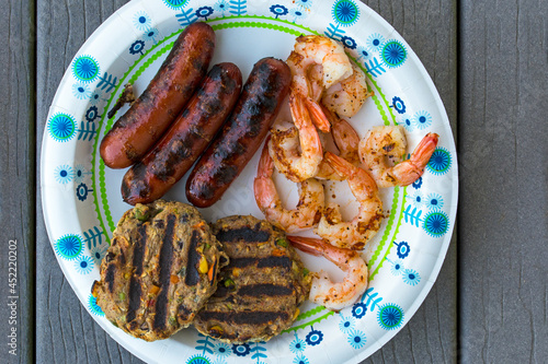 Casual backyard top view of grilled black bean veggie burger with turkey hotdog and spicy grilled shrimp on a paper plate photo