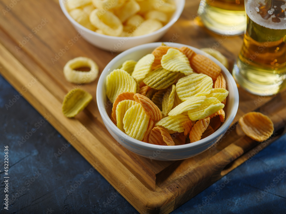 Light light beer in glasses and light snacks - potato chips, onion rings. on a wooden tray. Dark blue background. High angle view. Rest, relaxation, rest with friends or with family.