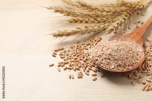 Wheat bran, kernels and spikelets on wooden table, closeup. Space for text photo