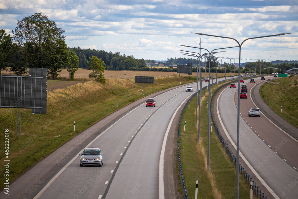 Beautiful view from above on highway road with several cars. Green side fields and blue sky background. Sweden. Beautiful view from above on highway road with several cars. Green side fields and blue sky background. Sweden.