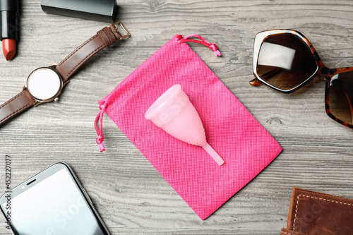 Menstrual cup and different women's accessories on wooden table, flat lay