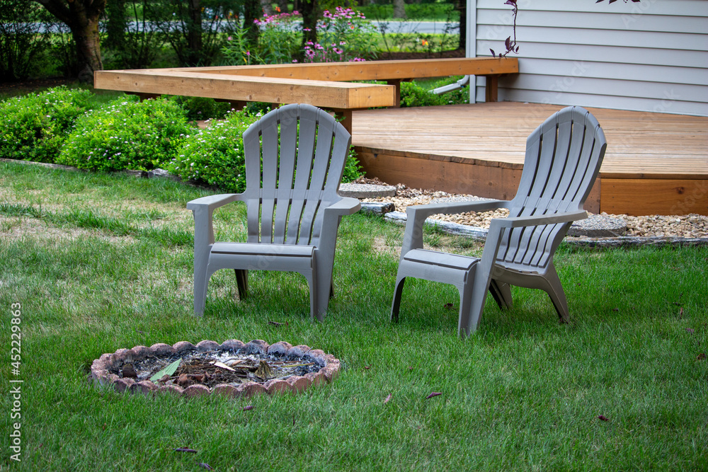 Close up view of a pair of gray lawn chairs in a back yard, near a fire pit, with light dappled shade Close up view of a pair of gray lawn chairs in a back yard, near a fire pit, with light dappled shade