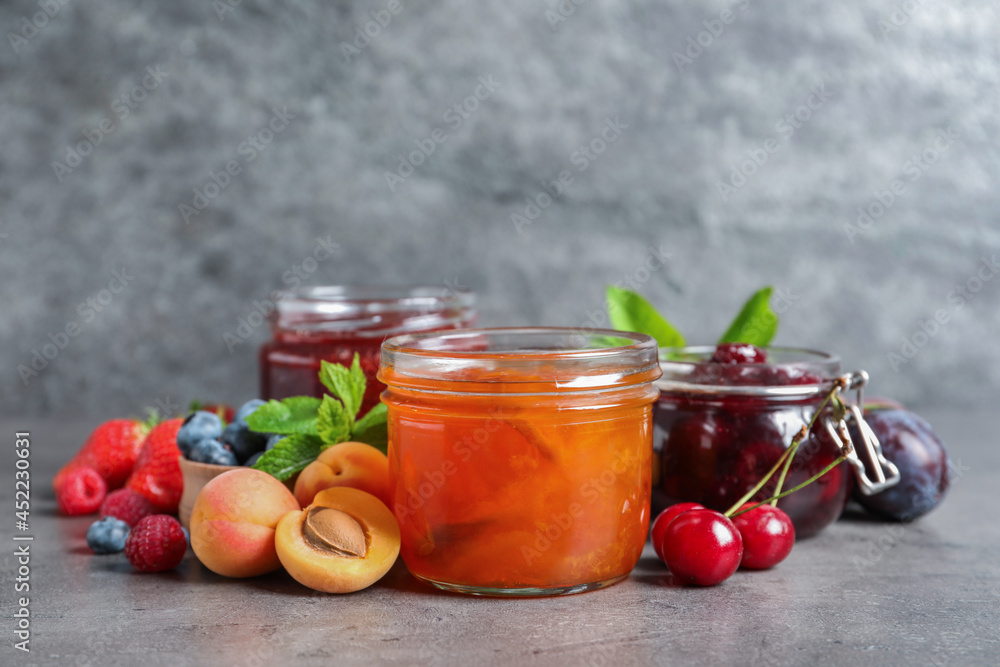 Jars with different jams and fresh fruits on grey table Jars with different jams and fresh fruits on grey table