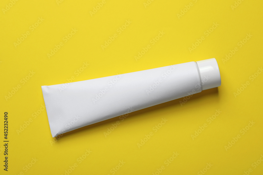 Blank tube of toothpaste on yellow background, top view