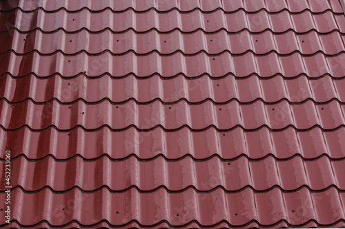 The roof of a private house with metal tiles of burgundy color.