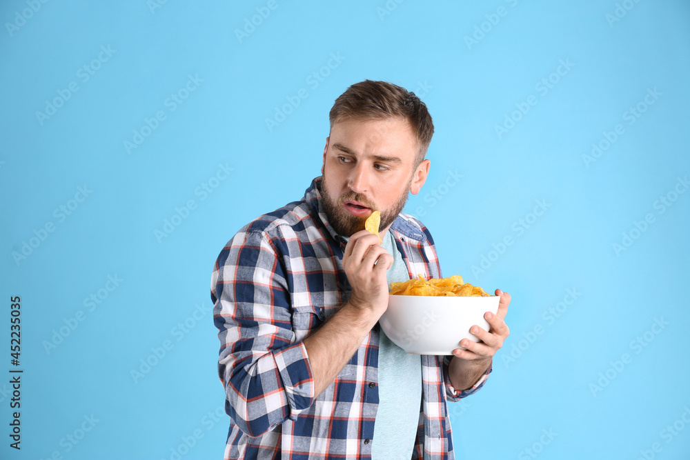 Greedy young man hiding bowl with chips on light blue background Greedy young man hiding bowl with chips on light blue background