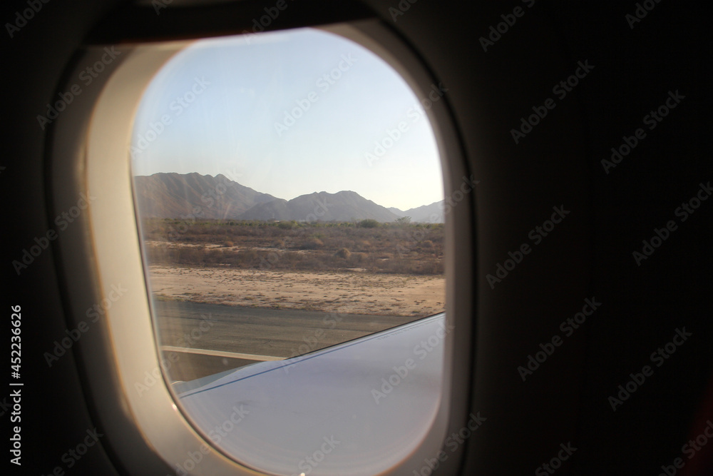 View from the window of an airplane where the wing is seen over the landscape of sea and mountains
