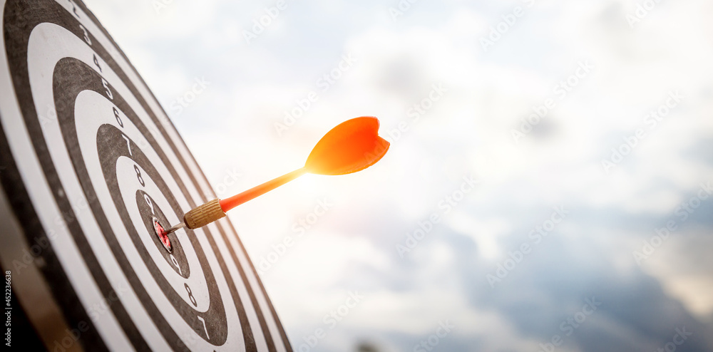 Close up shot red darts arrows in the target of dartboard center on dark blue sky background. Business target or goal success and winner concept. Close up shot red darts arrows in the target of dartboard center on dark blue sky background. Business target or goal success and winner concept.