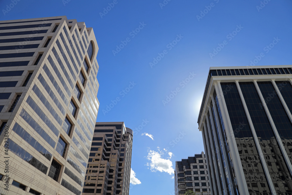 Tall business buildings are shown from a street level view during the day.