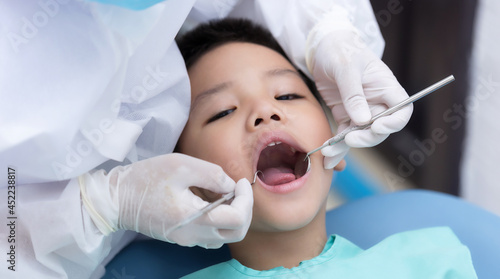 Dentist examining Asian little boy teeth in the clinic. Calm and happy