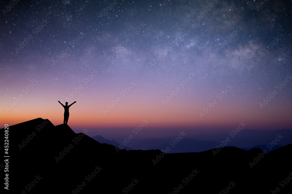Silhouette of young female traveler and backpacker watched the star and milky way alone on top of the mountain before sunrise. She enjoyed traveling and was successful when he reached the summit.