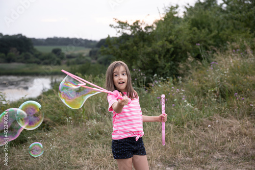 A little girl blows large, colorful soap bubbles in the nature.