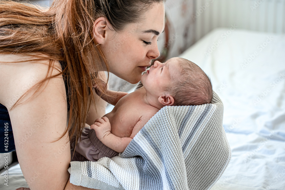 A young mother kisses her newborn son wrapped in a blanket. A young mother kisses her newborn son wrapped in a blanket.